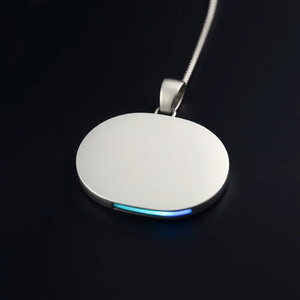 The ORRA Node: a brushed titanium pendant about 45 mm wide with a polished ceramic contact face, on a braided steel cord with a machined clasp.